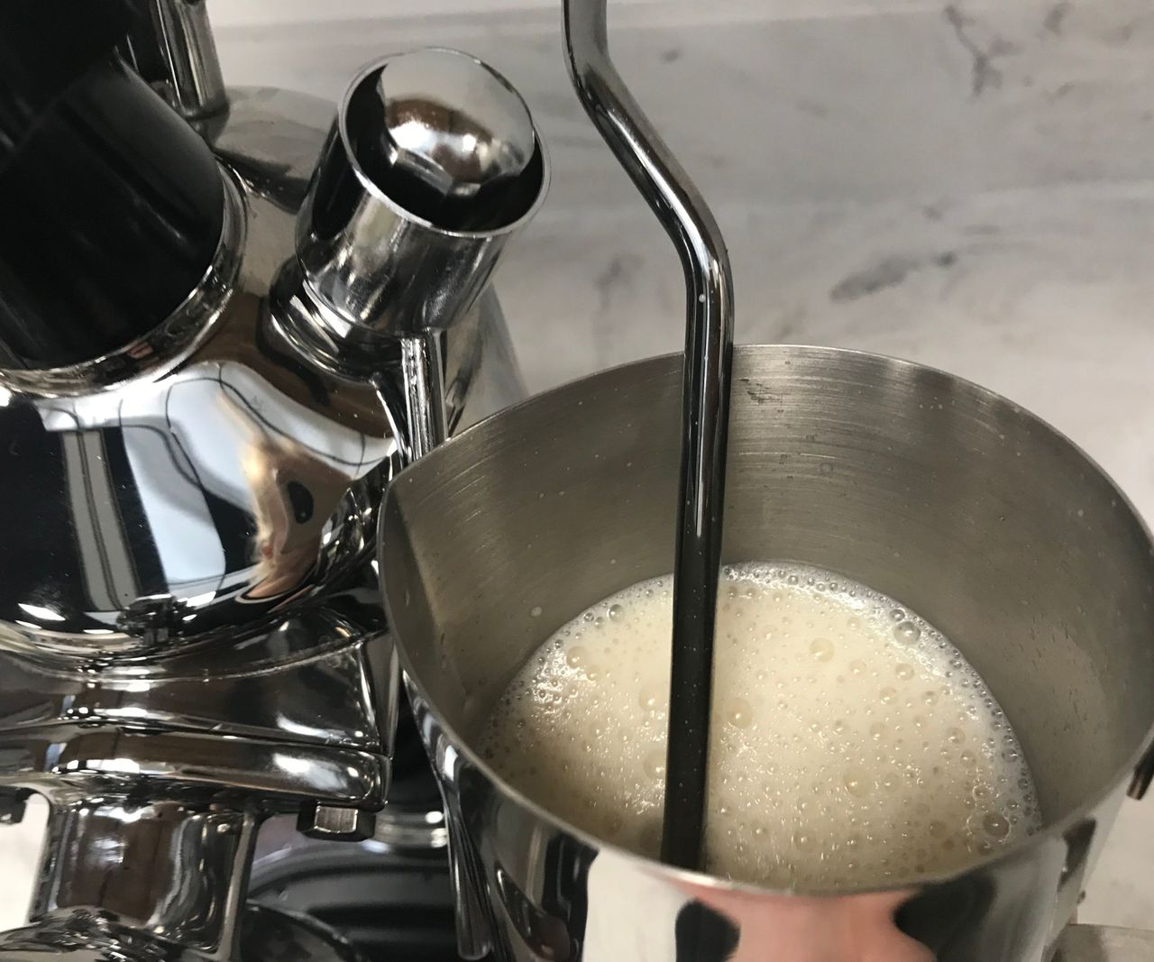 A close up of a milk steaming wand in a stainless steel cup of milk.