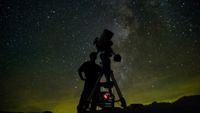 a silhouette of a person looking into a telescope under starry skies