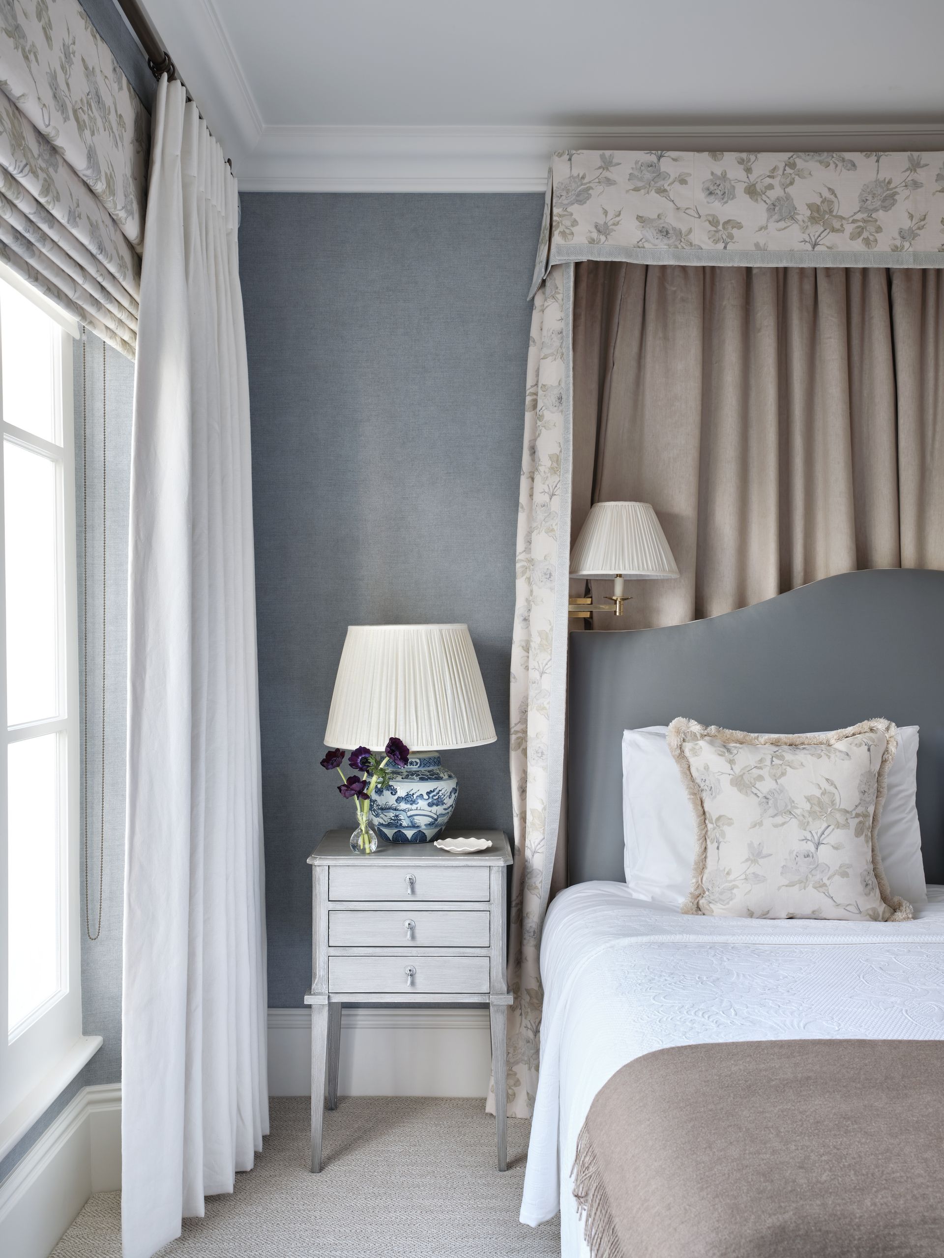 A bedroom with blue walls, a valance bed, and a floral patterned motif in the soft textiles
