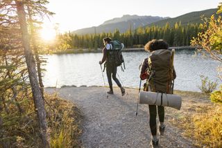 Two backpackers walking beside a lake