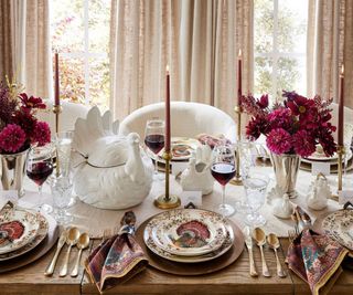 A wooden dining table decorated with harvest-themed plates and a turkey serving bowl