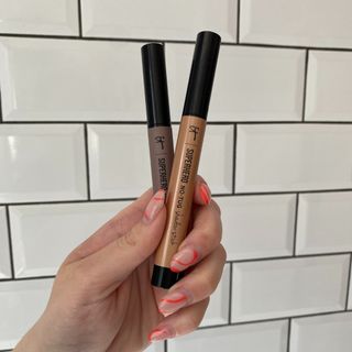 Original image showing hand holding two of the IT Cosmetics Superhero No-Tug Eyeshadow Sticks