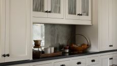 Close-up image of white kitchen cabinetry with black countertops. There are a couple of woven baskets on the counter with ceramic jars and produce in them