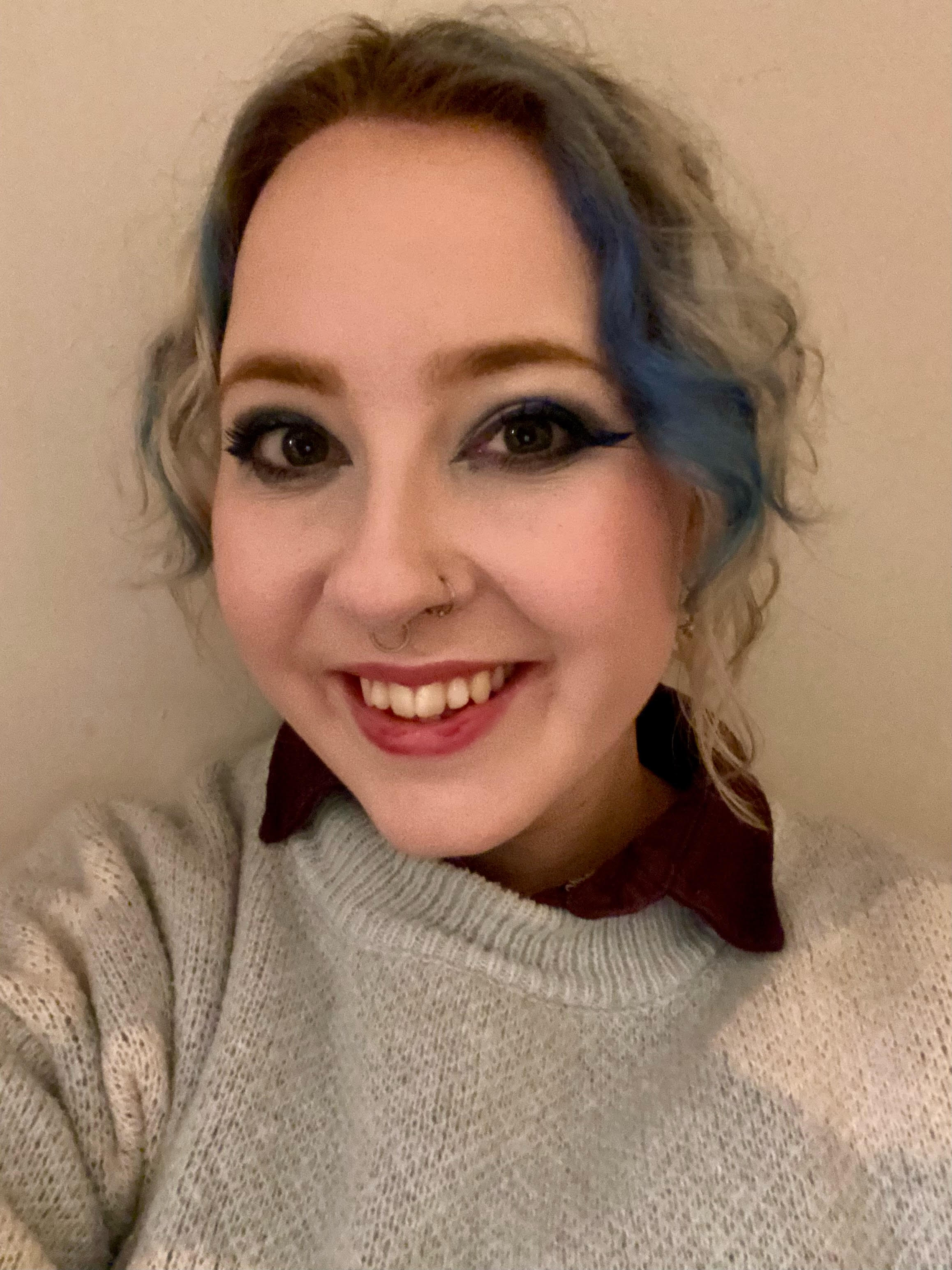 Olivia Powell, the Commissioning Editor for Tech Software at Tom' Guide, smiles at the camera. They are wearing a blue jumper and have blue and white hair.