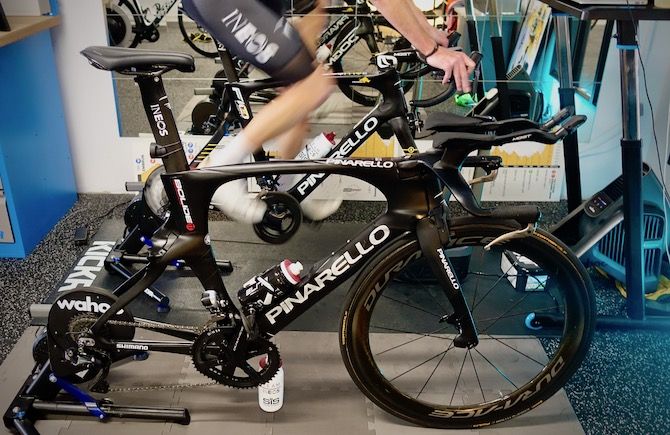 Chris Froome&rsquo;s Pinarello Bolide TT bike stands ready for a Zwift session while Froome spins out on his road bike
