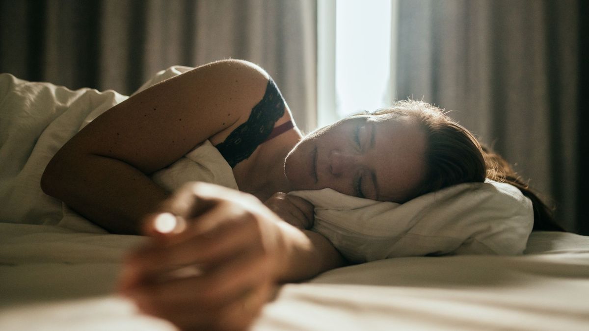 A woman sleeping on her side peacefully with the curtains open slightly letting some light in