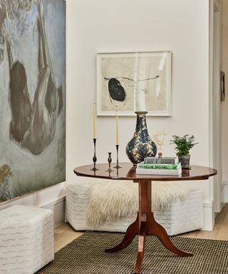 entryway with white walls large artwork antique pedestal table and cube bench seats