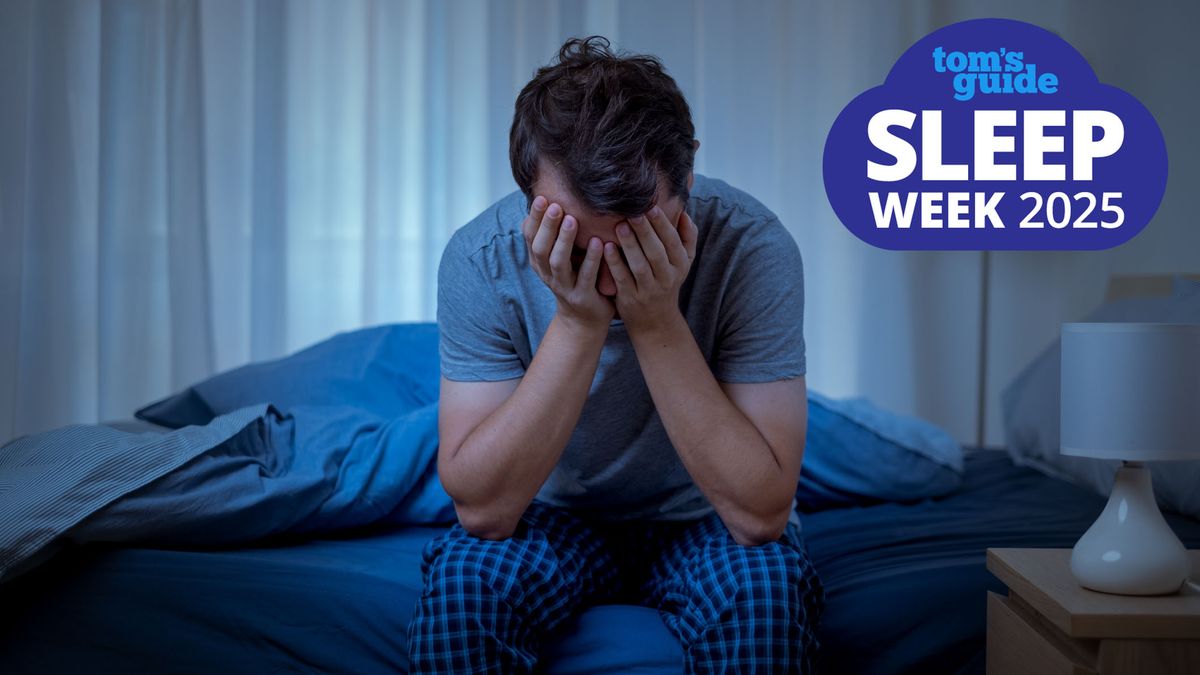 A man in a blue t shirt holds his head in his hands and sits on the edge of his bed because he can&#039;t sleep due to intrusive thoughts and needs to try cognitive shuffling for sleeping