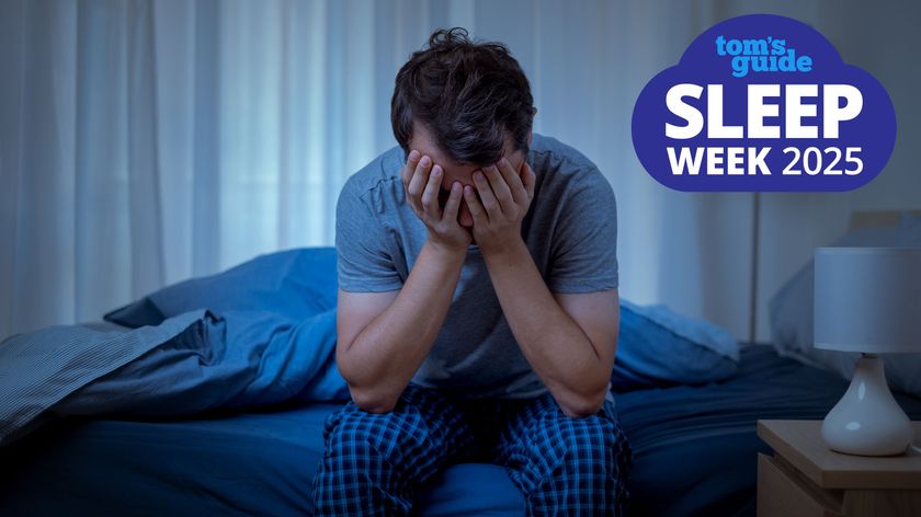 A man in a blue t shirt holds his head in his hands and sits on the edge of his bed because he can&#039;t sleep due to intrusive thoughts and needs to try cognitive shuffling for sleeping