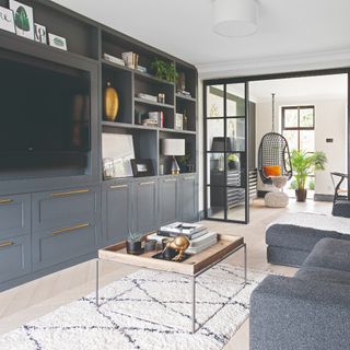 A living room with a TV within a media unit and a grey corner sofa