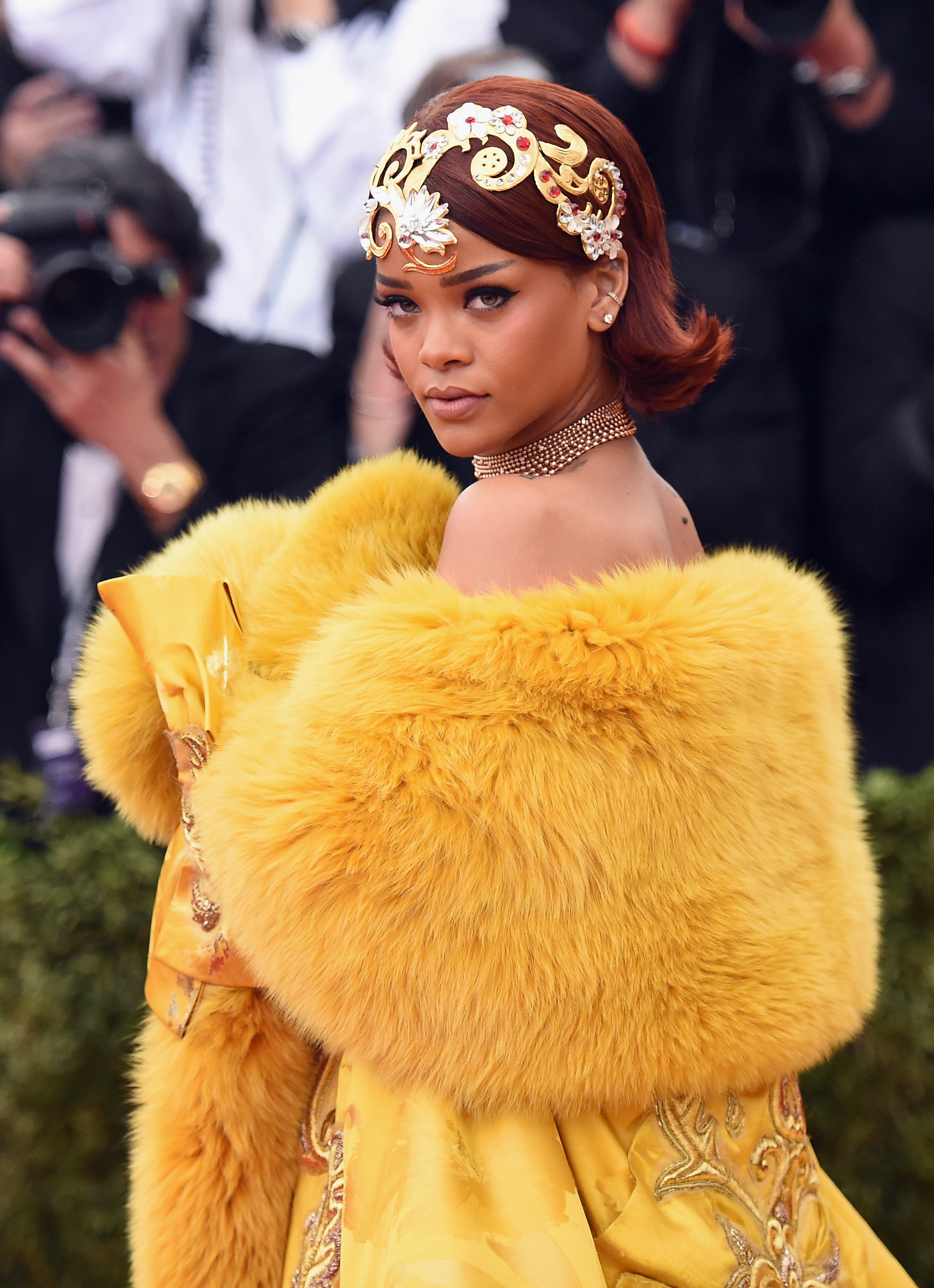 Rihanna wears a gold headpiece and a yellow fur cape.