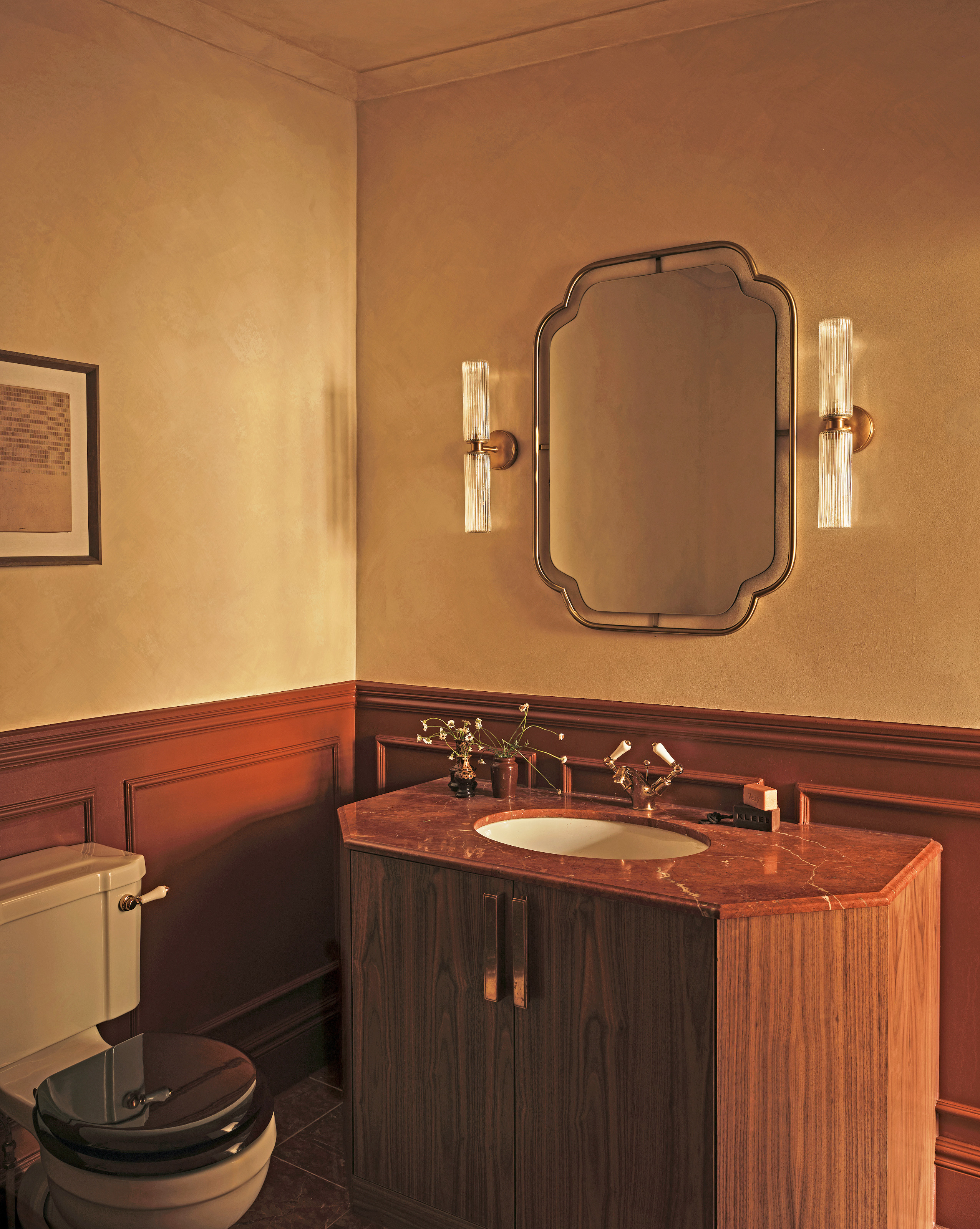 Bathroom with limewash walls and rust panelling, wood vanity with red marble top, Art Deco style mirror and glass wall lights