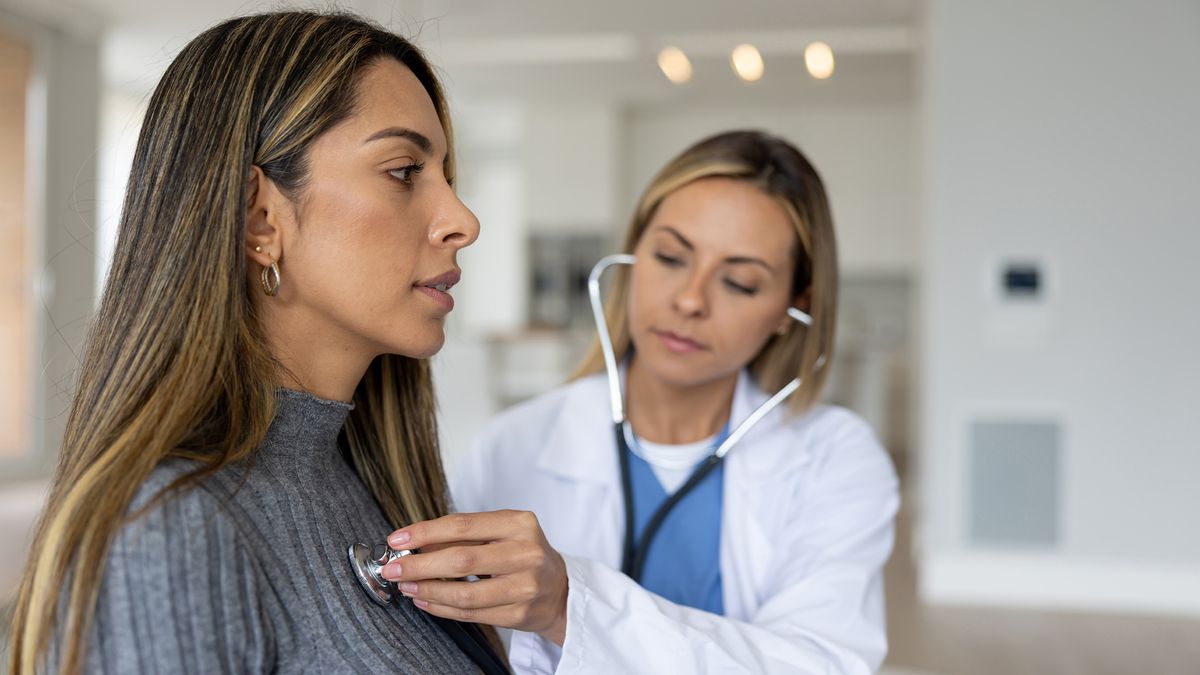 Doctor placing a stethoscope on a female patient&#039;s chest over the patient&#039;s sweater