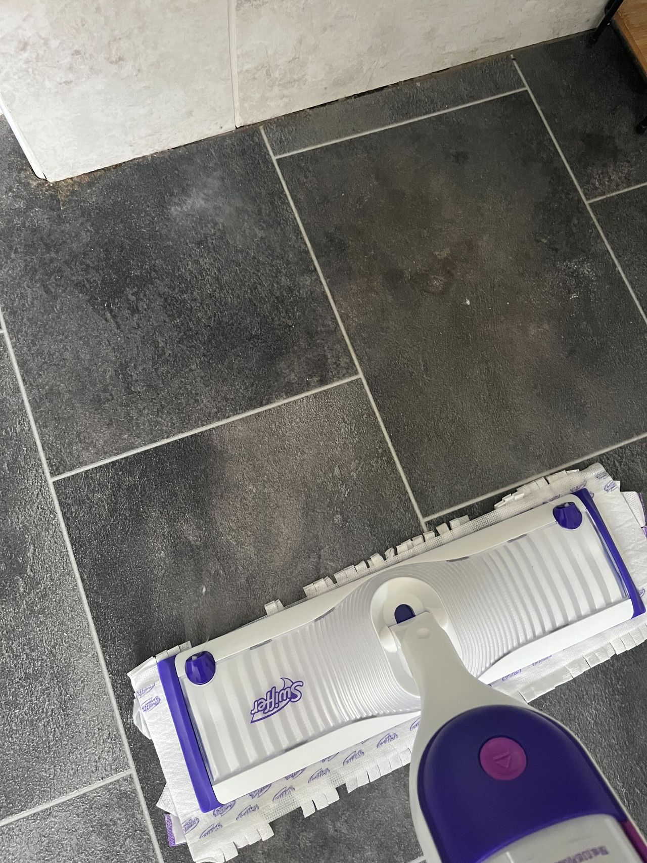 Using a purple and white Swiffer power mop to clean a bathroom floor