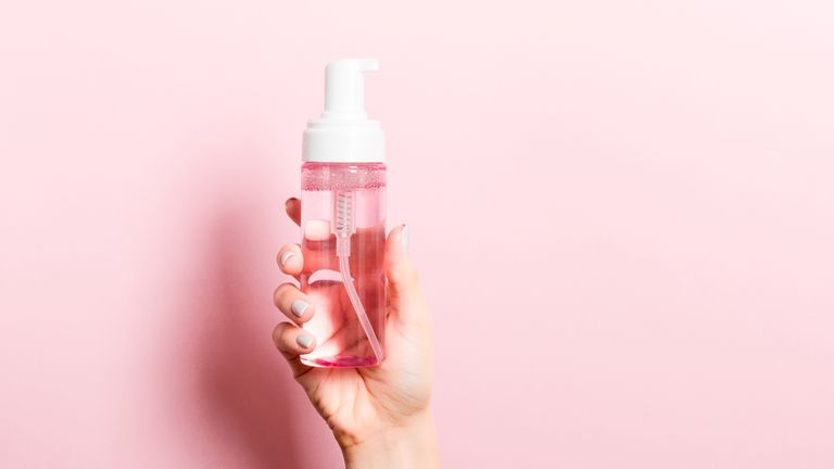 Clear pink skincare bottle held up against pink background