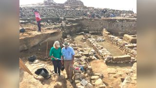 Researchers stand near the ruins of ancient walls, with the destruction layer about midway down each exposed wall.