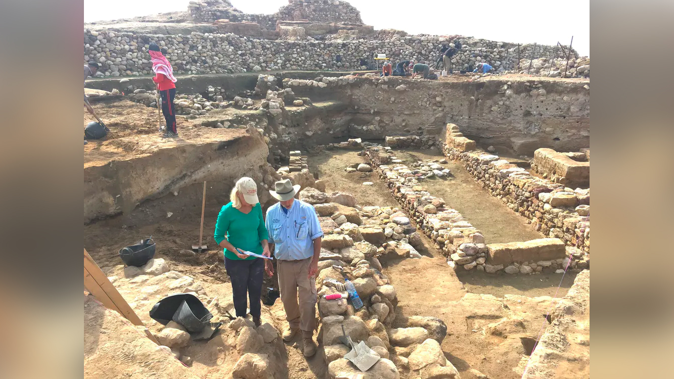 Die Forscher stehen in der Nähe der Ruinen alter Mauern, wobei die Zerstörungsschicht etwa in der Mitte jeder freigelegten Mauer liegt.