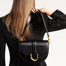 A woman facing away, holding a black Charles & Keith handbag over her shoulder.