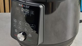 a black instant pot with a dial and touchpad is photographed against a blue background