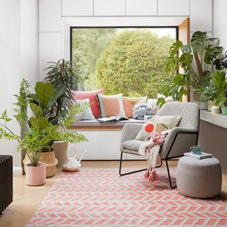 white living room with large window seat with cushions, an orange pattern rug, grey armchair and pot plants