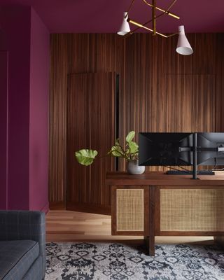 A home office with wine toned walls and wood flooring