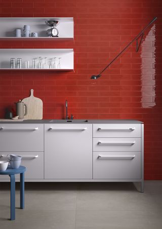 A white galley kitchen with stainless steel handles, red tiled wall with subway/metro tiles
