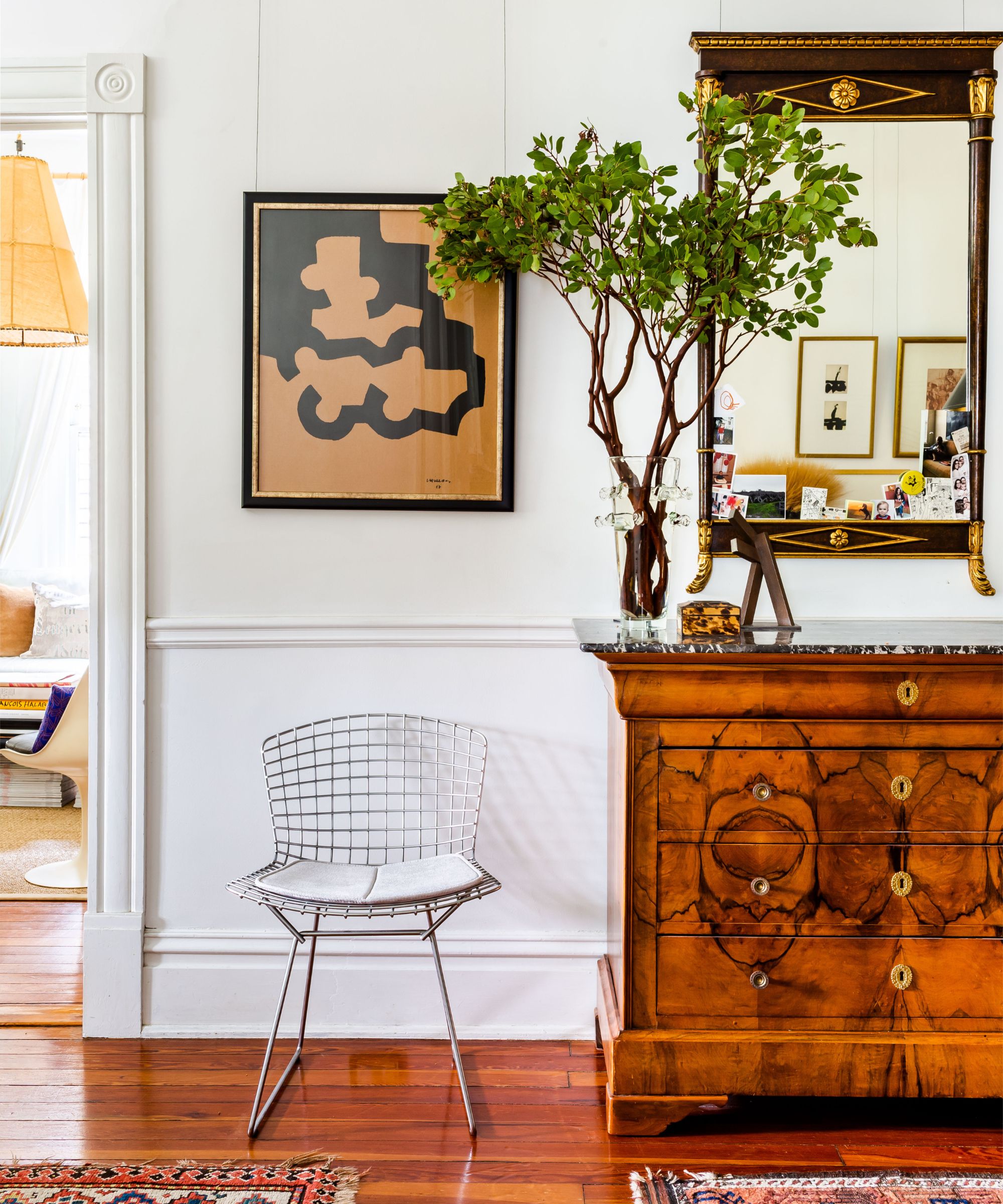 Mid-century Bertoia-style wire accent chair with a seat cushion, styled beside an antique wood chest and decorative mirror in a traditional living room.