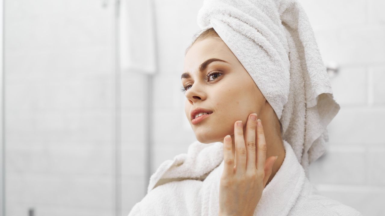 A woman applies face cream in her bathroom