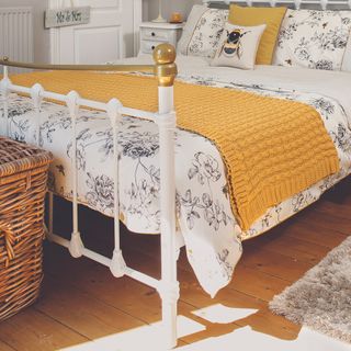 A white metal bedframe with a yellow knitted throw