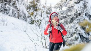 A woman in a red coat hikes through the trees in the snow