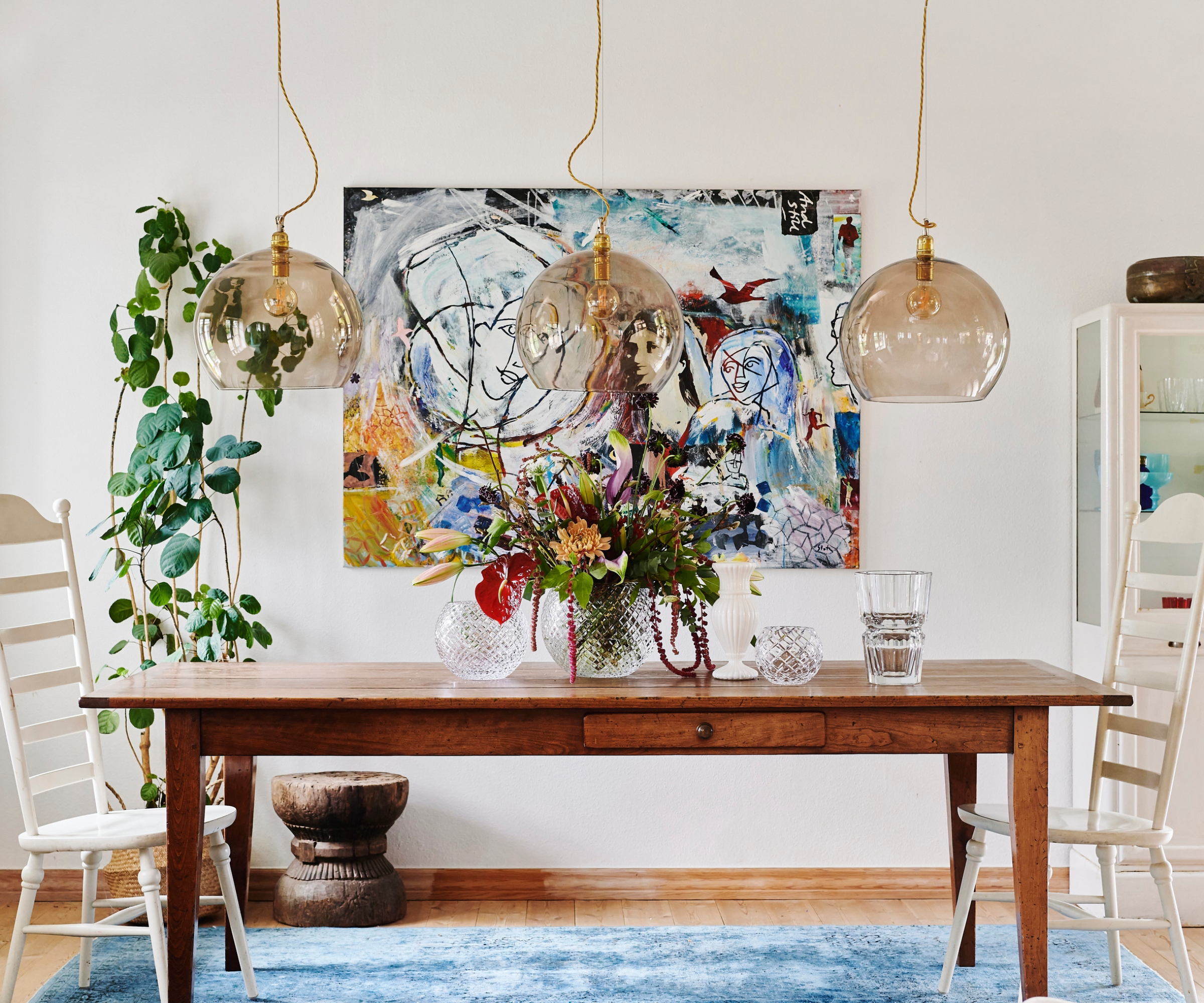 3 brown smoked glass pendants hanging above wooden dining table with vibrant artwork on the wall behind
