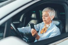 Woman looking at her phone while parked in a car.