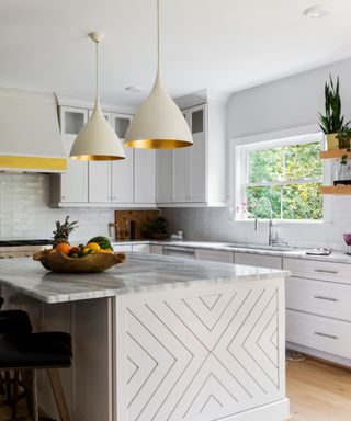 White kitchen with small white island, marble countertops, pendant lights with copper inside