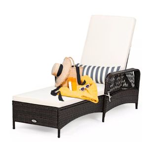 A black rattan chaise lounge chair with a white cushion and a bag with a hat on it