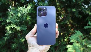 En mørkeblå mobiltelefon av typen iPhone 14 Pro Max holdes i en hånd.
