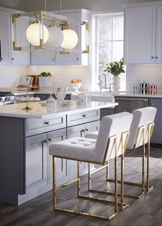 White kitchen ideas with wall cabinets, kitchen worksurface and kitchen island stools, and gold accents in the lighting and bar stools.
