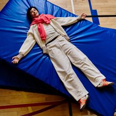 Model lying on a school sports mat wearing BAM athleisurewear and orange trainers sold at BAM