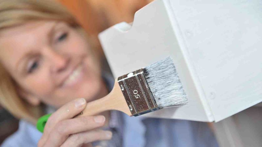 A female decorating wood furniture using a paint brush and Osmo white wood finish