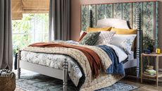 A bedroom with large bed topped with assortment of soft furnishings including duvet, throw and pillows with green decorative headboard