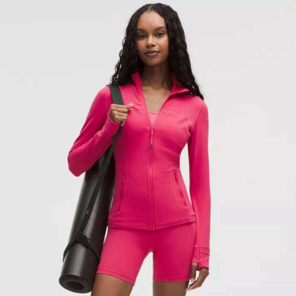 Young woman wearing bright pink lululemon workout set whilst holding black yoga mat