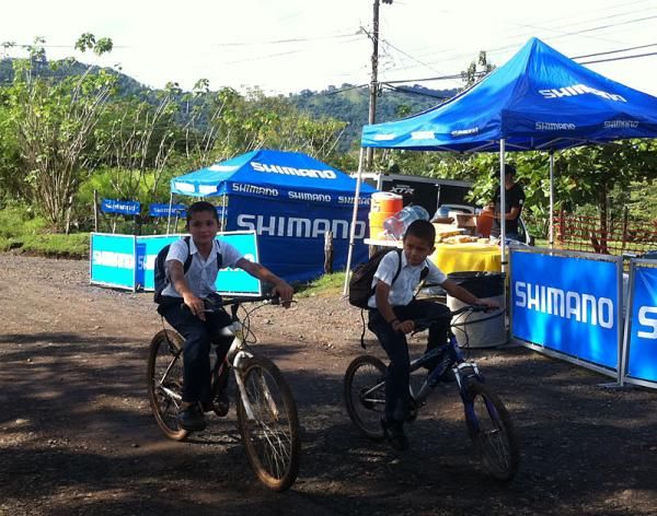 Two schoolchildren ride through an aid station.