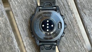 The bottom of the titanium Garmin Fenix 8, showing the charging port, QuickFit watch band connectors, and etched info about the watch