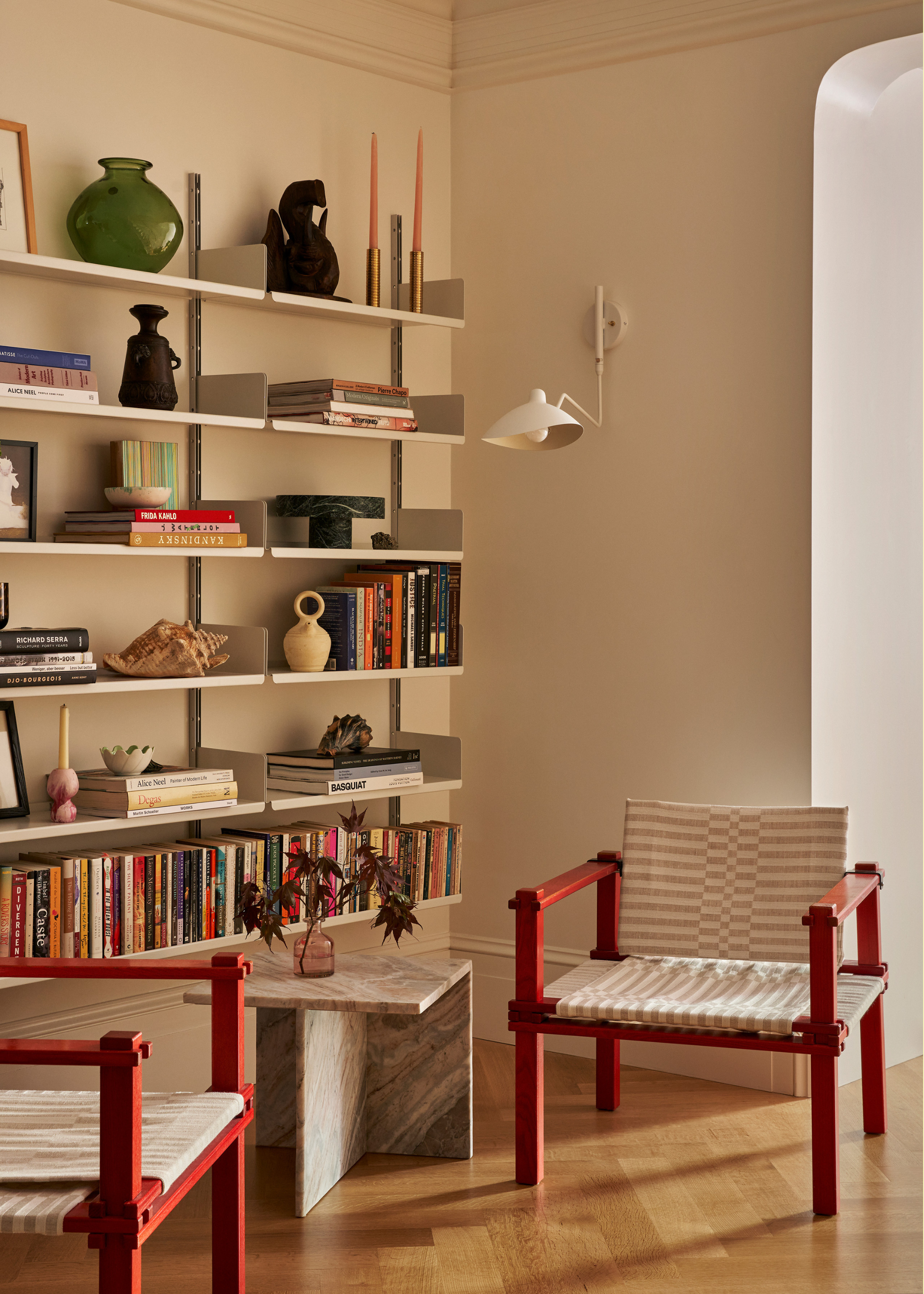 A reading corner with floating bookshelves a pair of chairs, a stone side table and a white wall sconce
