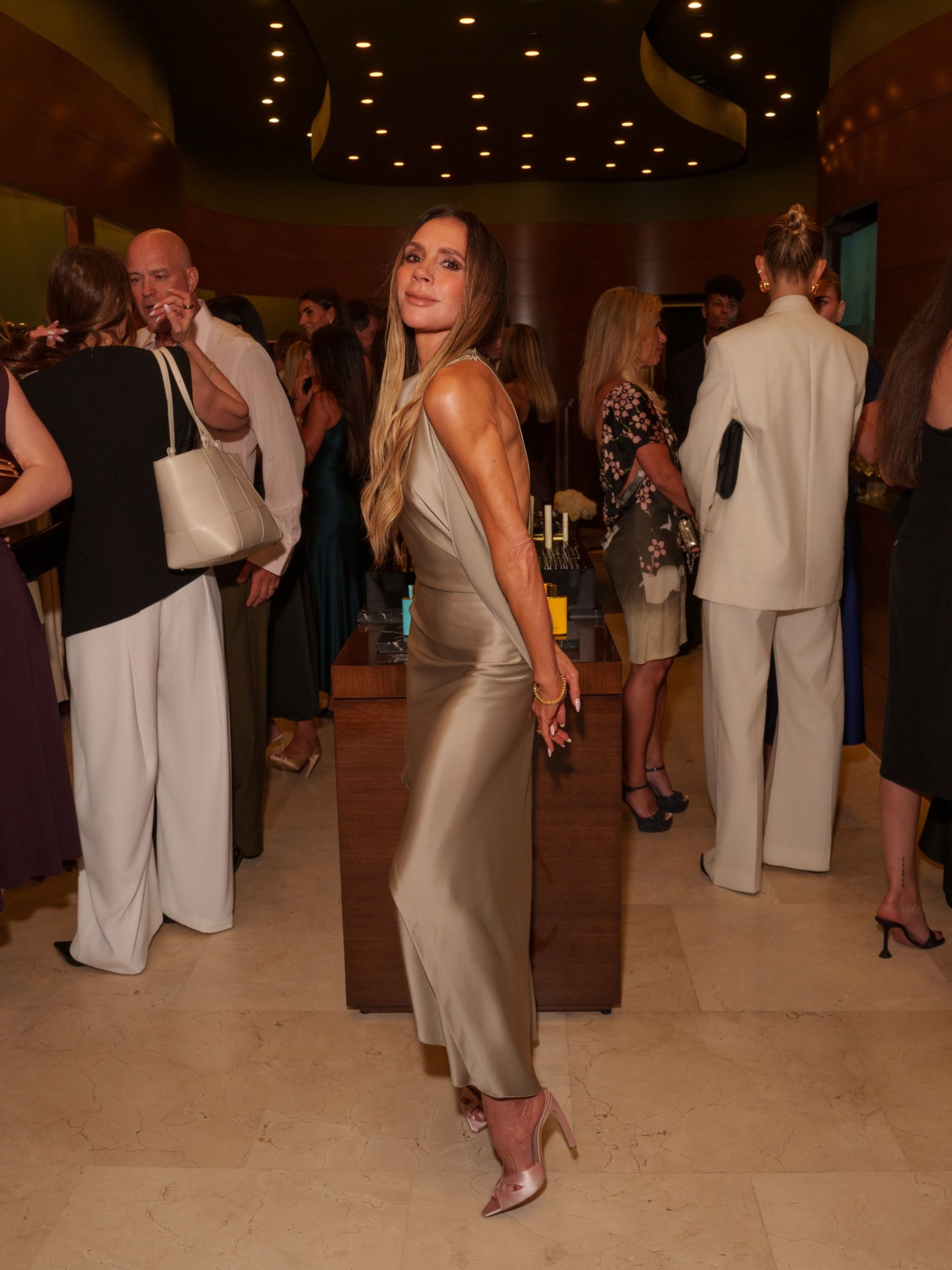 Victoria Beckham wears a neutral dress with pink satin heels.