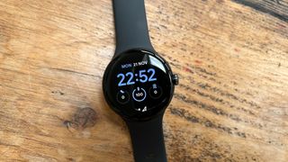 The Google Pixel Watch with a black strap laid on a table