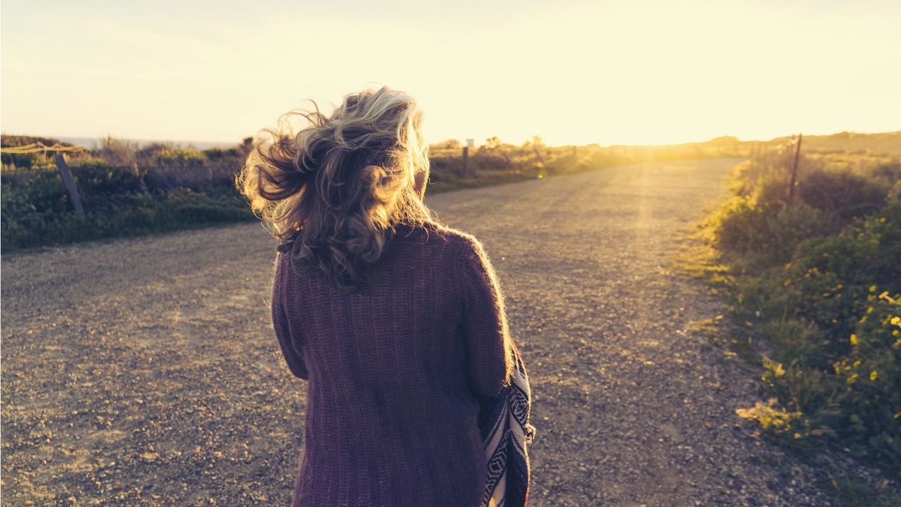 An older woman walks toward a sunset.