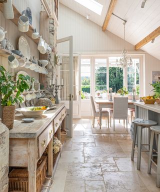 Long and narrow kitchen diner extension with stone tiled floor, large kitchen dresser and french doors beyond dining table