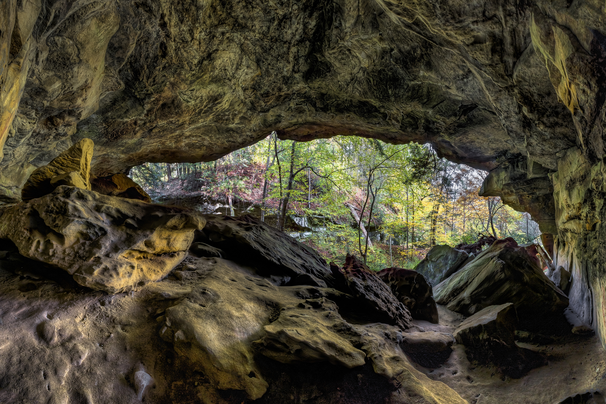 An overhanging cliff forms a large recess cave looking out onto the colors of autumn at Piatt Park in Monroe County, Ohio.