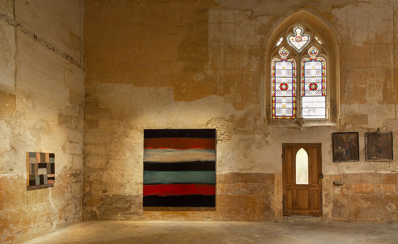 View of the &#039;Celtique&#039; exhibition by Sean Scully at Château de Boisgeloup - multicoloured paintings by Scully in a space with distressed walls, a wooden door and a stained glass window