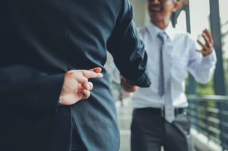 Businessman crossing fingers while shaking someone's hand